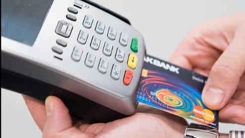 sleek merchant payment, focused, swiping card, photorealistic, bustling market background with colorful stalls and shoppers, highly detailed, dynamic motion blur effect of card swipe, shallow depth of field, vibrant colors, soft warm lighting, shot with a 50mm lens.